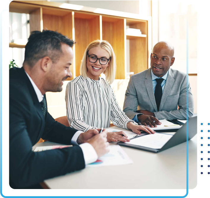 Three diverse businesspeople smiling and discussing paperwork together during a meeting around a boardroom table in a bright office